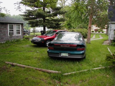 1997 Ford Taurus - Two sedans are parked in a residential yard with trees and houses visible.