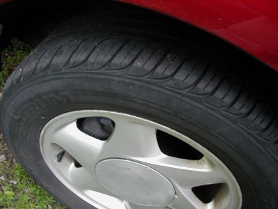 1997 Ford Taurus - Close-up of a car tire and wheel, with part of the red car body visible.