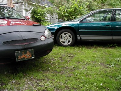 1997 Ford Taurus - Two sedans are parked on a grassy area, with trees and a house in the background.