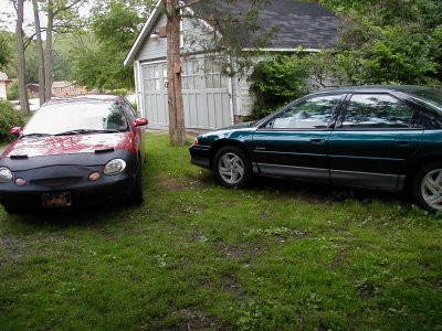 1997 Ford Taurus - Two sedans, one red and one green, are parked on a lawn in front of a garage.