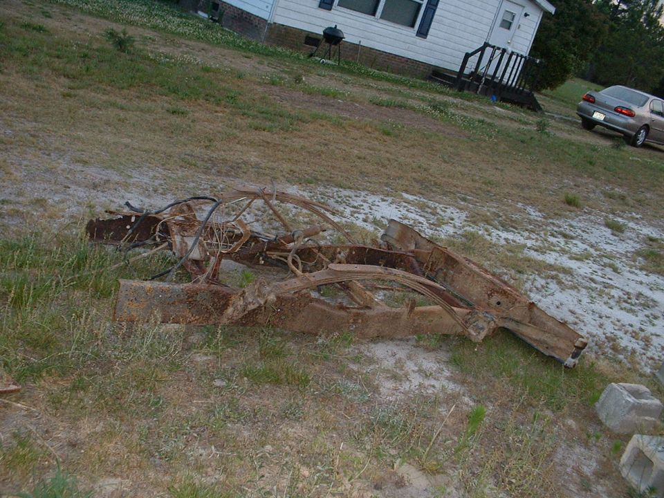 rusted car frame lying on grass in front of a house