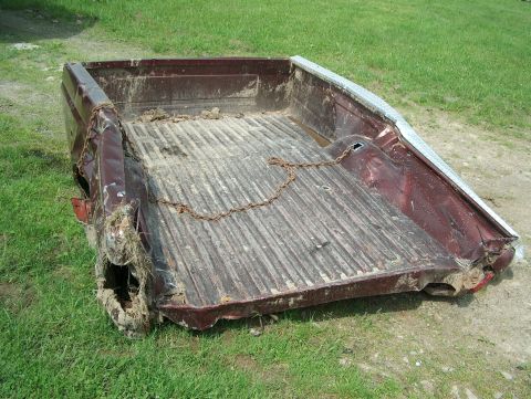 1990 Ford F-150 - A damaged truck bed sits on grass, showing significant wear and tear on its rear sections.