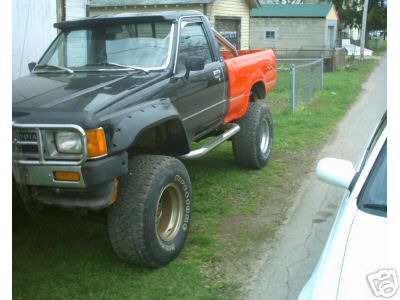 1986 Ford F-150 - This pickup truck features a two-tone paint scheme with an orange bed and black cab, equipped with large off-road tires.