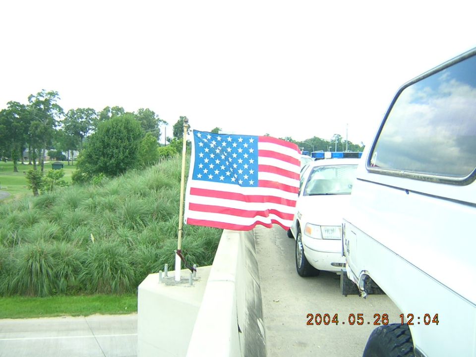 American flag on pole next to white vehicles, one with blue lights