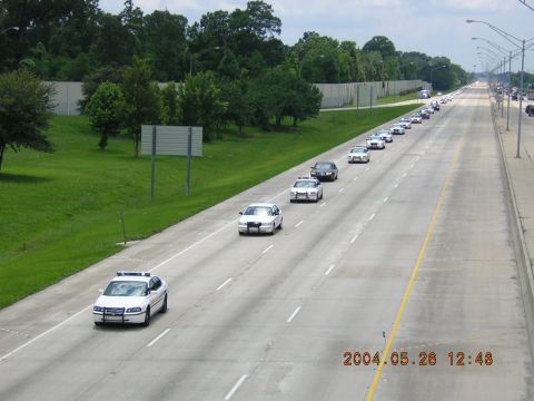 1984 Chevrolet Blazer - A long line of police vehicles travels down a highway under a cloudy sky.