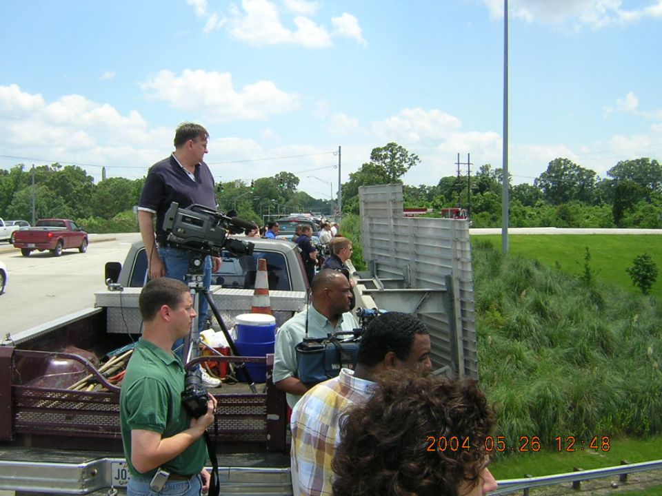 Pickup truck bed with people holding cameras, a red truck in the background, and a traffic scene