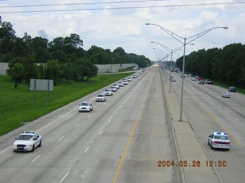 1984 Chevrolet Blazer - A long line of police cars drives down a highway, likely for a funeral procession.