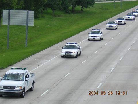 1984 Chevrolet Blazer - Multiple white police cars and a security truck are driving in a convoy on a highway.