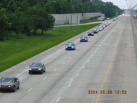 1984 Chevrolet Blazer - A procession of vehicles, including several police cars, travels down a highway.