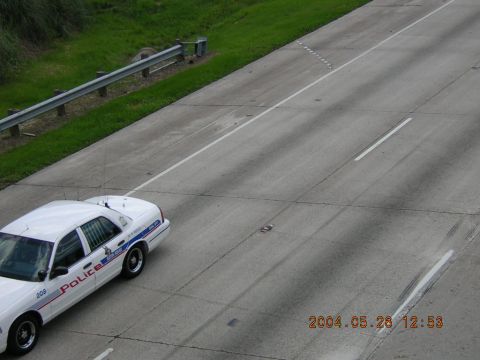 1984 Chevrolet Blazer - A white police car drives on a highway, captured from an elevated perspective.