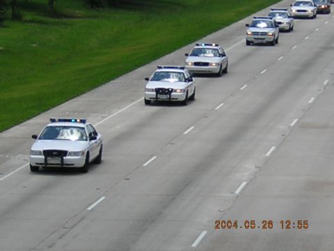 1984 Chevrolet Blazer - A line of police cars drives down the highway, likely as part of a funeral procession.