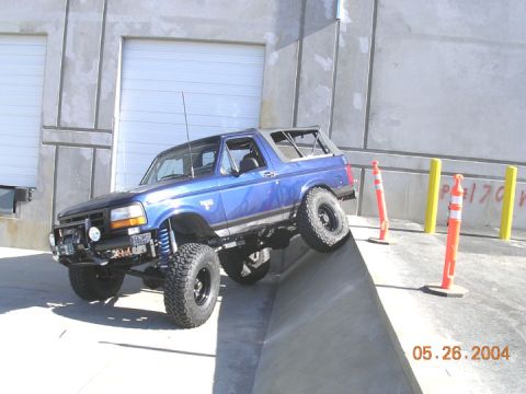 1994 Ford Bronco - Blue 1994 Ford Bronco with lifted suspension is shown off-roading on a concrete ramp.