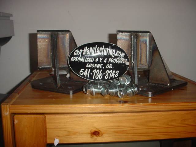 Pair of bare steel 4x4 brackets with bolts and a Sky Manufacturing sticker on a wood dresser