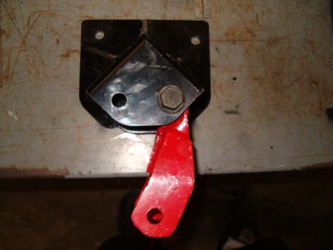 1988 Ford Bronco - A red metal bracket is bolted to a black metal plate, likely a vehicle part.