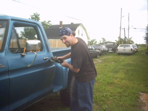 1991 Ford LTD Crown Victoria - Man works on the door of a blue pickup truck while other vehicles are parked in the yard.
