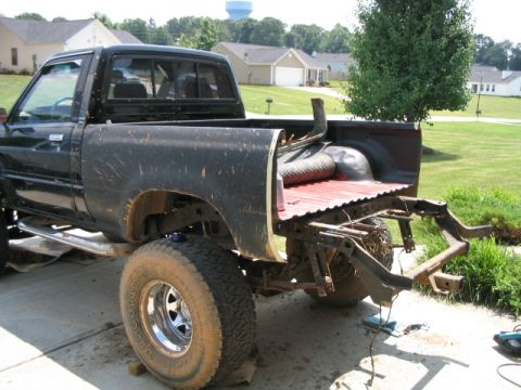 1986 Ford F-150 - This black pickup truck is viewed from the rear, showing its bed removed and the exposed frame, indicating it is undergoing repairs or modi…