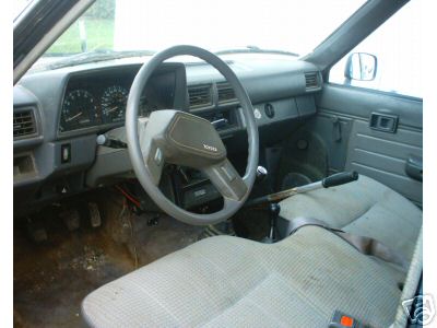 1986 Ford F-150 - Interior of a Toyota truck, likely from the 1980s, with manual transmission and worn seats.