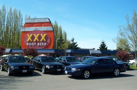 1995 Ford Crown Victoria - Several dark sedans are parked in front of a XXX Root Beer establishment. The closest vehicle appears to be a 2000 Ford Crown Victoria.