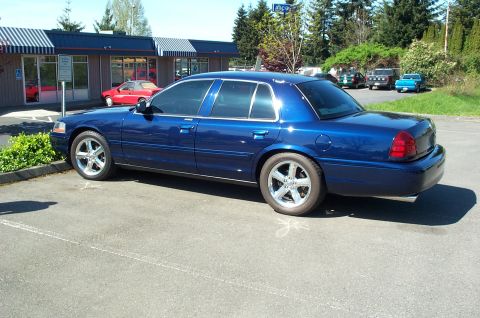 1995 Ford Crown Victoria - Blue sedan parked in a lot with a building and trees in the background.