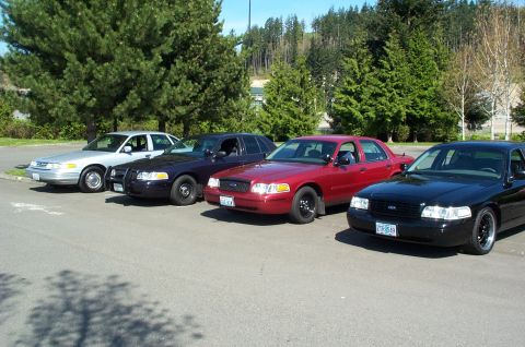 1995 Ford Crown Victoria - A lineup of four Ford Crown Victoria police interceptors are parked in a lot on a sunny day.