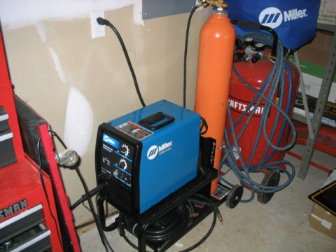 1986 Ford F-150 - Welding equipment including a Miller machine, gas cylinder, and air compressor are arranged in a garage setting.