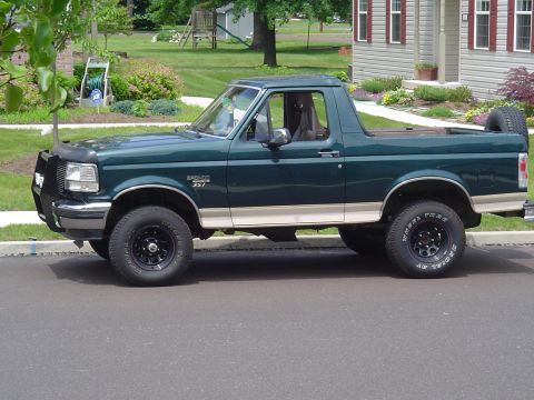 1993 Ford Bronco - This green Ford Bronco is parked on a residential street with a house and yard in the background.