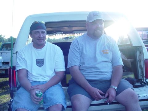 1989 Ford Bronco - Two men sit in the open tailgate of a white pickup truck, with another truck visible behind them.
