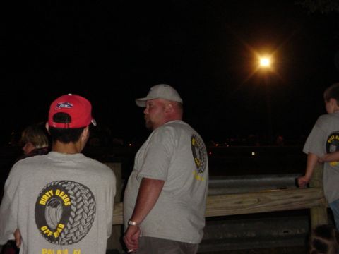 1989 Ford Bronco - Three individuals are seen at night, two of whom are wearing t-shirts with a tire graphic and the words 'Dirty Deeds Off Road'.