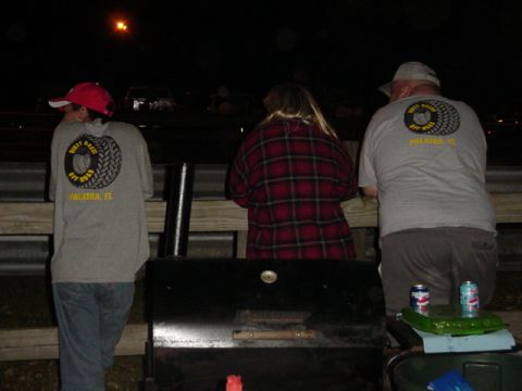 1989 Ford Bronco - People gather at night, with a grill visible in the foreground and cars in the background.