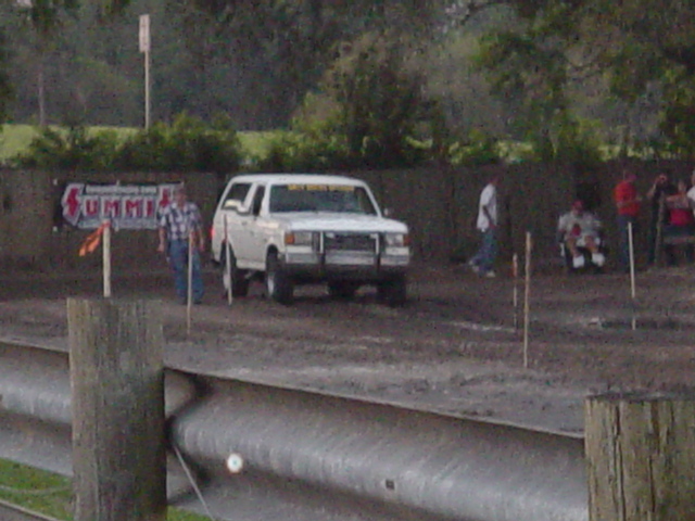 White Ford Bronco staged at a muddy truck-pull track with a Summit banner and spectators