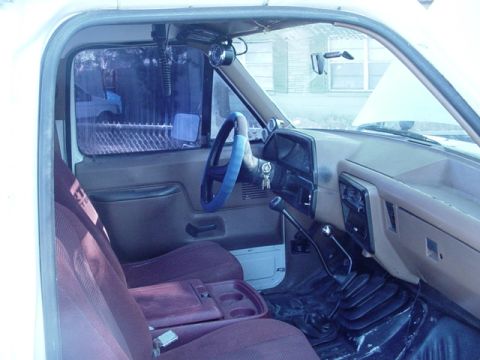 1989 Ford Bronco - The interior of a pickup truck is shown, a blue steering wheel cover and a manual transmission.