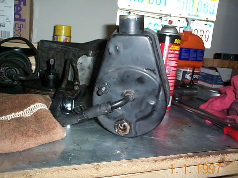 1992 Ford Bronco - A power steering pump is shown on a workbench with various automotive fluids and tools in the background.