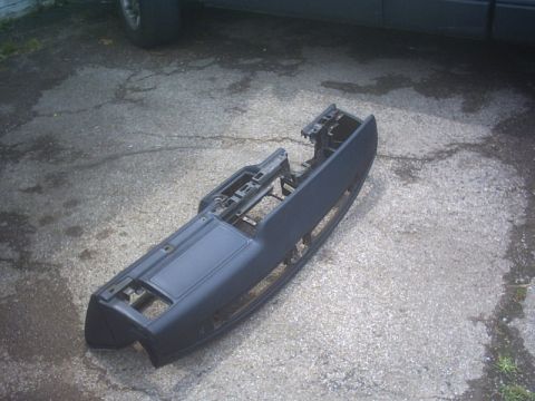 1991 Ford LTD Crown Victoria - A bare dark grey dashboard pad and frame removed from a car and laid face-up on a cracked asphalt driveway, with the glovebox door, defrost…