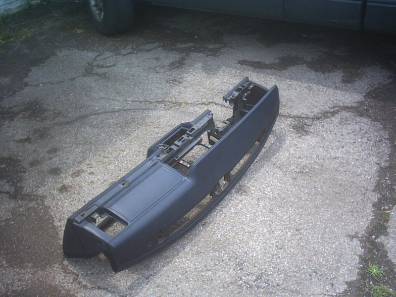 Bare grey dashboard removed from a car, laid on asphalt with glovebox and vent openings