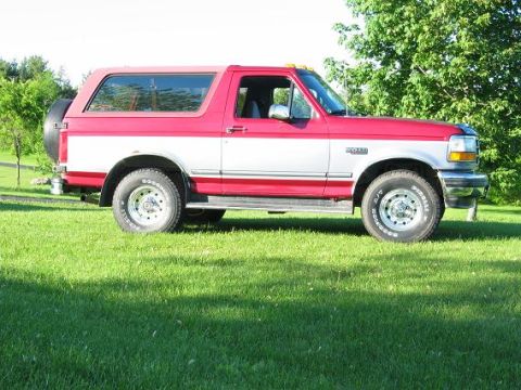 1995 Ford Bronco - A red and silver Ford Bronco is parked on a grassy lawn with trees in the background.