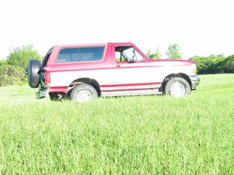 1995 Ford Bronco - This 1995 Ford Bronco is parked in a grassy field, showing its side profile and external spare tire.
