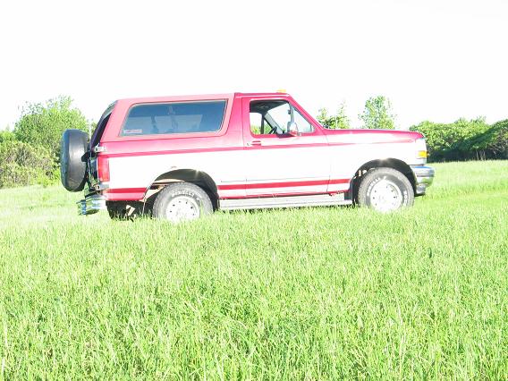 Red and white 1995 Ford Bronco side view with spare tire on rear