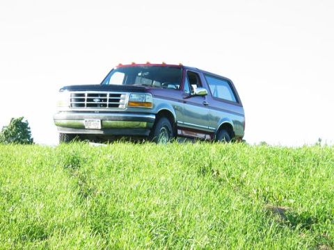 1995 Ford Bronco - 1995 Ford Bronco parked on a grassy hill under a bright sky.