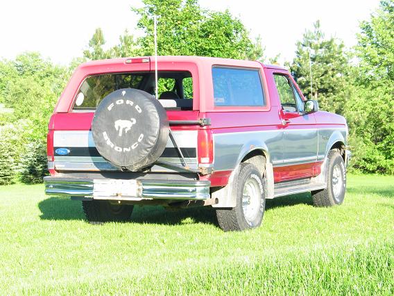 Red and silver Ford Bronco with a spare tire on the back, parked on grass