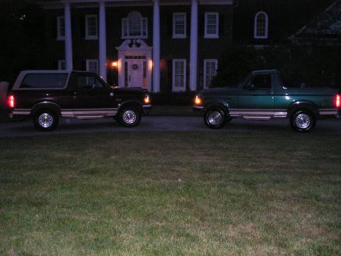 1996 Ford Bronco - Two SUVs are parked in front of a large house at night.