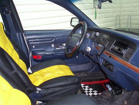 1995 Ford Crown Victoria - The interior of the vehicle features custom yellow and black seat covers and a wood-grain trim on the dashboard.