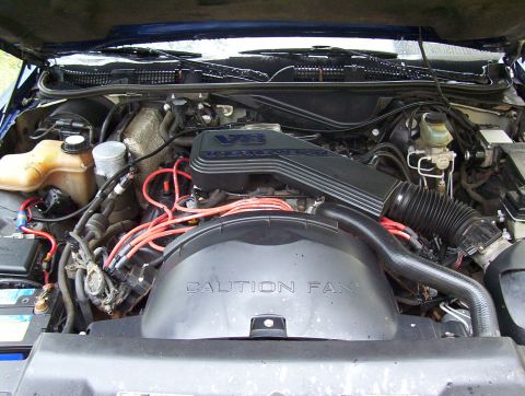 1995 Ford Crown Victoria - The engine bay of a blue 1995 Ford Crown Victoria is shown, the V8 engine and a caution fan shroud.