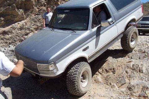 1992 Ford Bronco - A two-tone Ford Bronco navigates a rocky off-road trail with another vehicle in the background.
