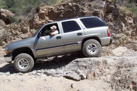 1992 Ford Bronco - A silver SUV navigates a challenging rocky off-road path with a driver visible behind the wheel.