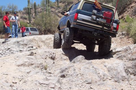 1992 Ford Bronco - A lifted 1992 Ford Bronco navigates a challenging rocky terrain, with other vehicles and people observing the off-road adventure.
