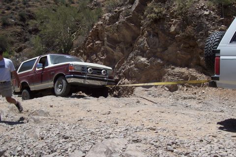 1992 Ford Bronco - A maroon and white Ford Bronco is stuck on a rocky trail, with a yellow tow strap attached to another vehicle.