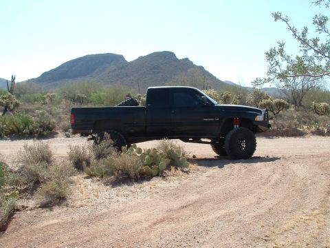 1990 Ford Bronco - Lifted black Dodge Ram 1500 pickup truck in a desert setting with mountains in the background.