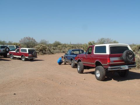 1990 Ford Bronco - Several off-road vehicles are parked in a desert landscape under a clear blue sky.