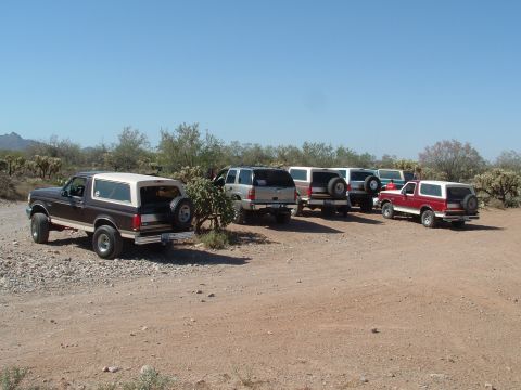 1990 Ford Bronco - Several SUVs and a Ford Bronco are parked in a desert landscape under a clear blue sky.