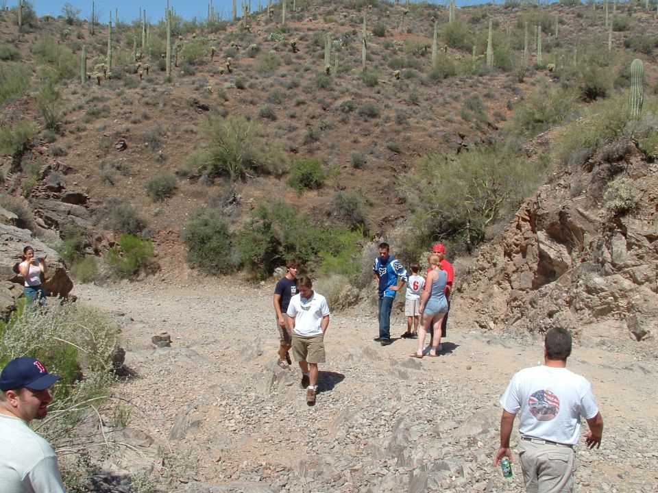Group of people walking down a rocky, dry desert wash with saguaro cacti on the hillside